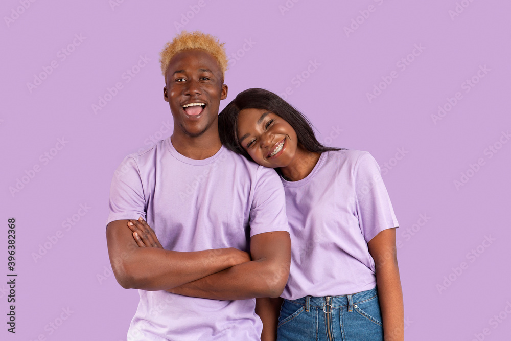Cheerful black woman putting head on her boyfriend's shoulder, expressing affection on lilac studio background Cheerful black woman putting head on her boyfriend's shoulder, expressing affection on lilac studio background