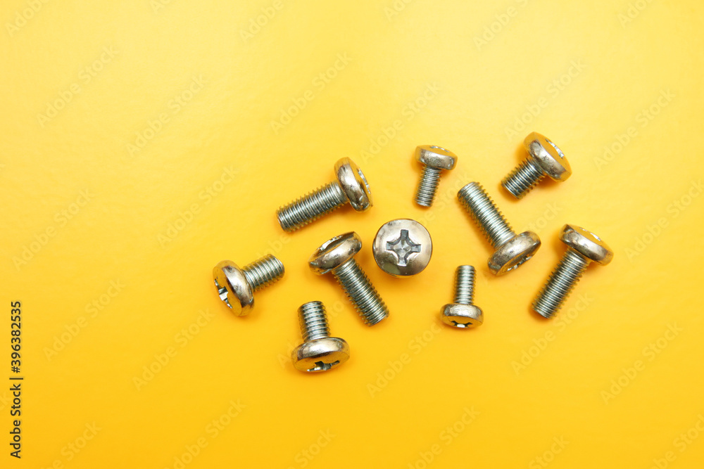Metal drywall screws on a yellow background, top view, cross screw cap Metal drywall screws on a yellow background, top view, cross screw cap