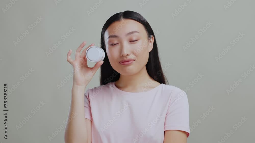 Young attractive asian woman holding cosmetic products showing at camera posing advertising background. Beauty cosmetics. Studio portrait. Young attractive asian woman holding cosmetic products showing at camera posing advertising background. Beauty cosmetics. Studio portrait.