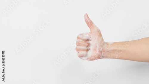 Hand with foam soap bubbles doing a like or thumbs up hand sign on white background.