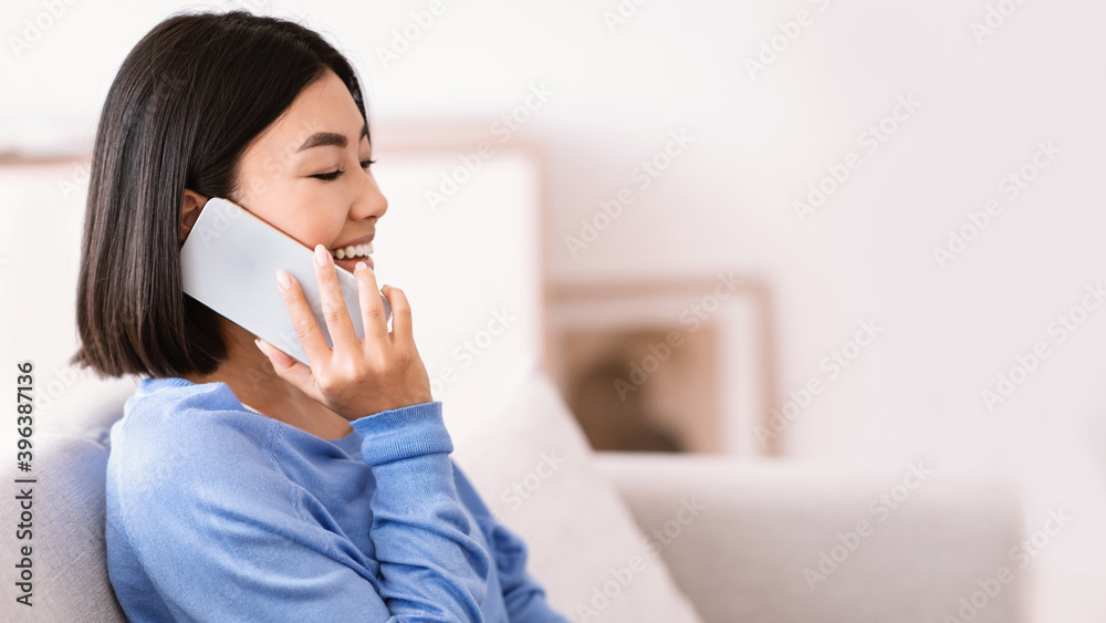 Smiling asian woman talking on phone sitting on couch Smiling asian woman talking on phone sitting on couch