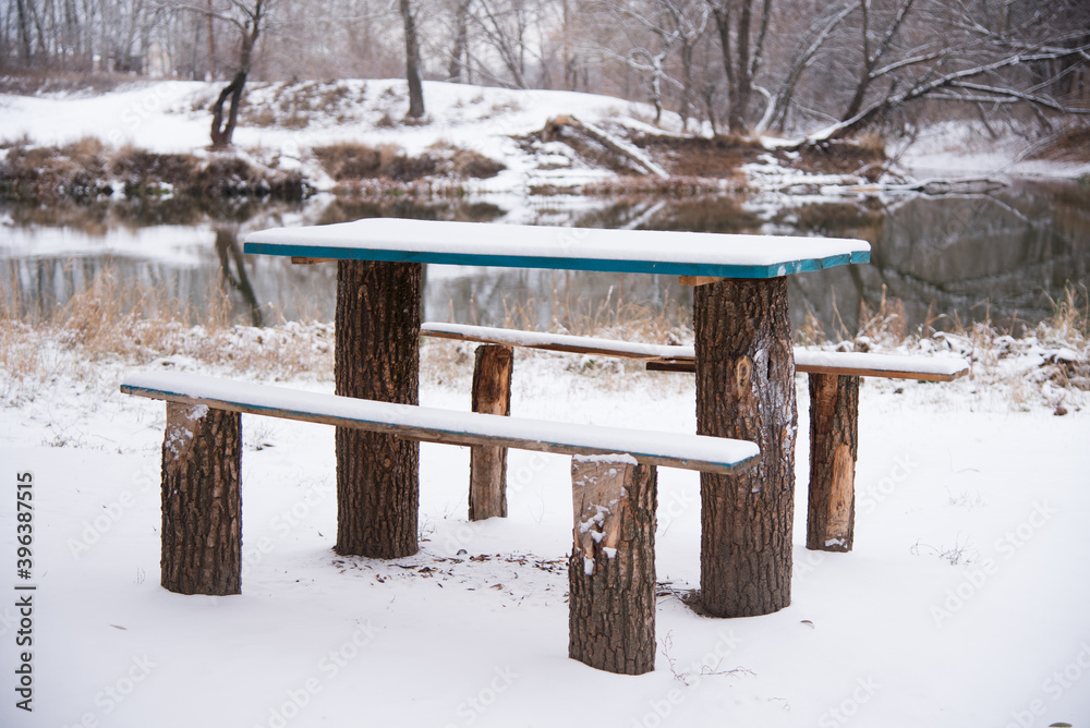 Bench and table are covered with snow, a resting place on the banks of the river in winter