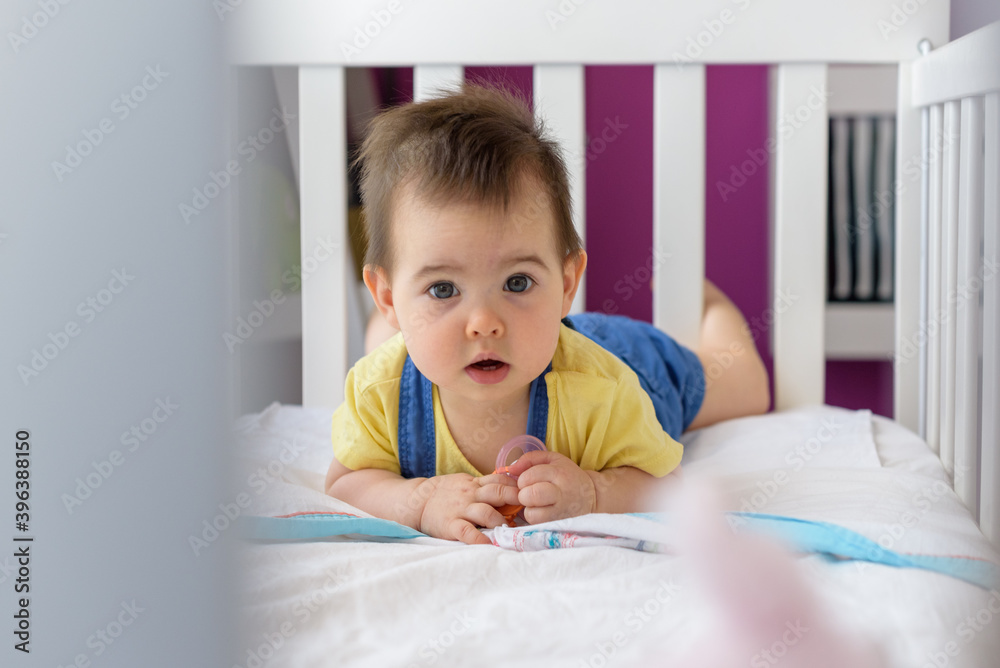 Bebé simpático tumbado boca abajo en cuna blanca con camiseta amarilla en hogar