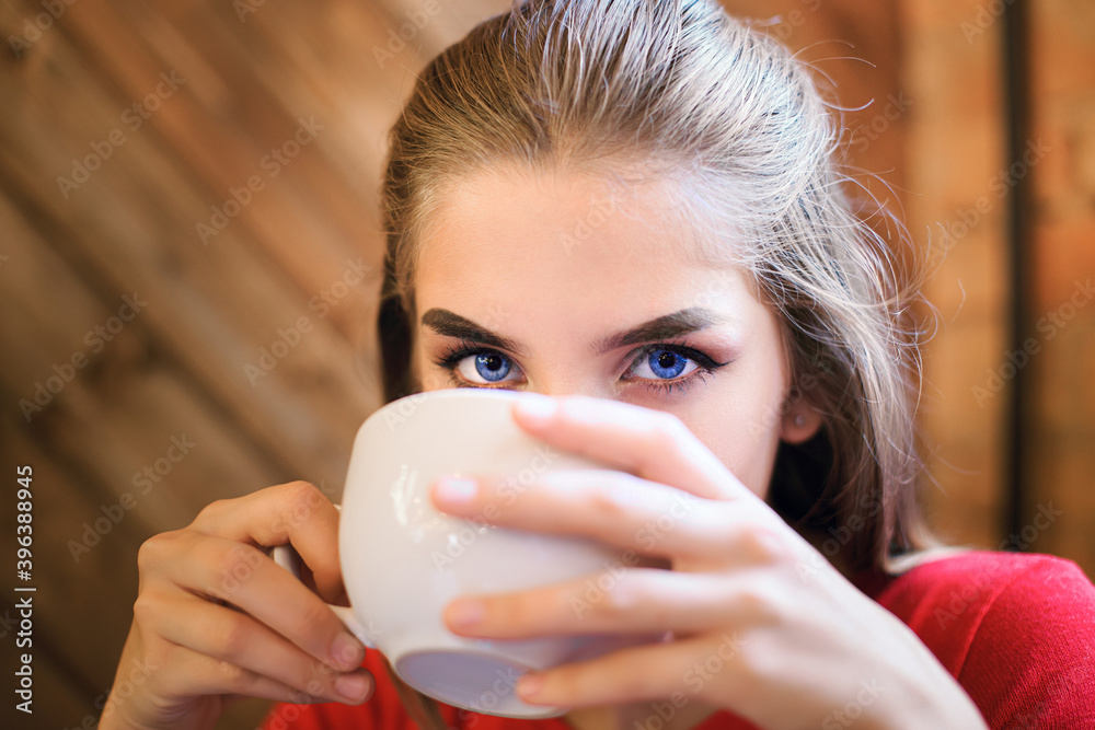 Portrait of a young blue-eyed woman in red in a cafe with a cup of tea or coffee Portrait of a young blue-eyed woman in red in a cafe with a cup of tea or coffee