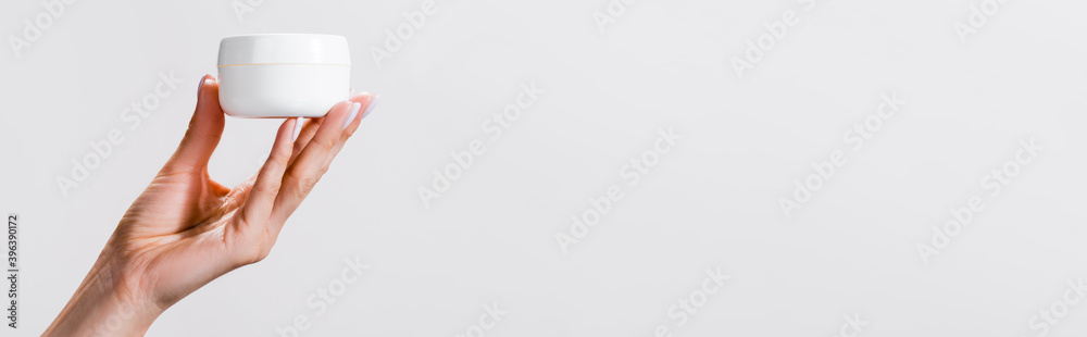 cropped view of woman holding container of hand cream isolated on grey, cropped view of woman holding container of hand cream isolated on grey,