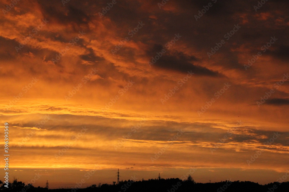 red and yellow sky, with the setting sun, waves of flaming clouds and dark shadows of trees and forests in the background