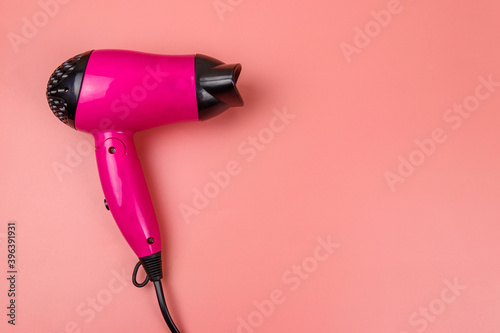 Pink hair dryer on a pastel pink background. Top view