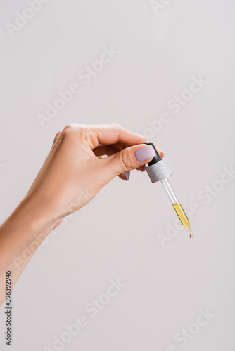 cropped view of woman holding pipette with oil isolated on grey, stock image
