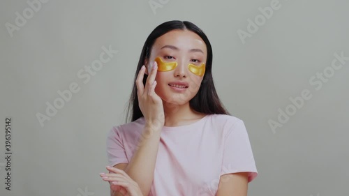 Chinese beautiful sensual woman in pink T-shirt wearing patches under eyes doing facial anti-aging treatment. Dark circles. Female beauty. Cosmtics. photo