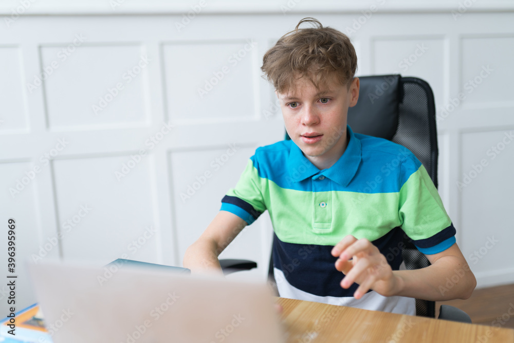 Cute Caucasian teen boy is attending his online lessons sitting in his room. Remote education concept during coronavirus lockdown Cute Caucasian teen boy is attending his online lessons sitting in his room. Remote education concept during coronavirus lockdown