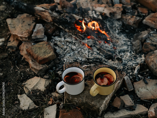 Two metal mugs with mulled wine stand near the fire. Autumn picnic.