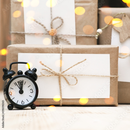 hand made christmas gifts wrapped in craft paper and alarm clock. bokeh lights. christrmas celebration time. sustainable holiday gifts. photo
