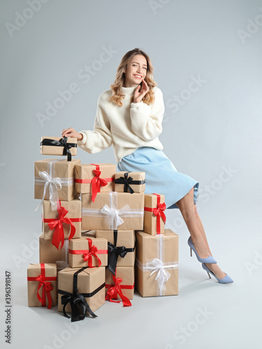 Beautiful young woman with pile of Christmas presents on light grey background