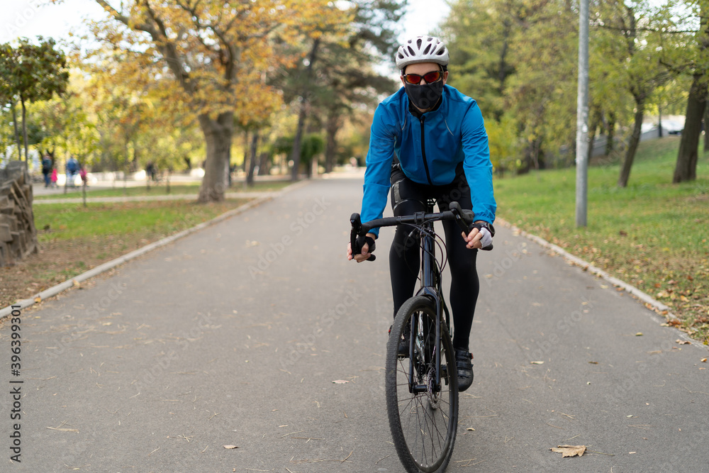 A man in a protective mask and helmet rides a bicycle on the road. Active rest in quarantine. Fighting excess weight.