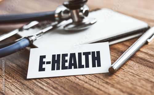 E-HEALTH. Word written on card on wooden table with medical background.