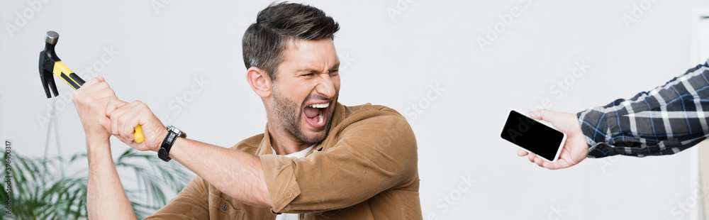 Obraz premium Angry businessman with hammer shouting near smartphone in hand of man, banner