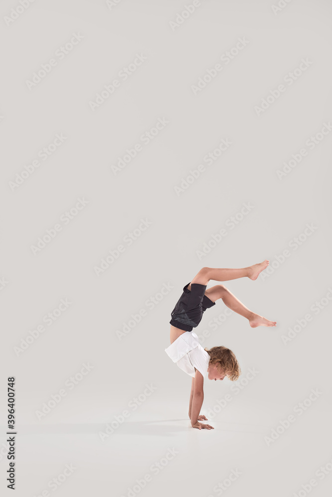 Fototapeta premium Full length shot of little playful boy child standing on his arms with legs in the air isolated over grey background