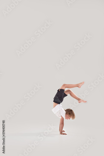 Full length shot of little playful boy child standing on his arms with legs in the air isolated over grey background