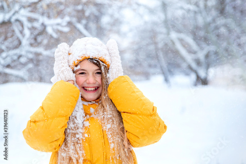 Outdoor portrait of young smiling girl, wearing yellow jacket in winter park