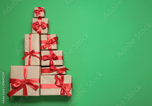 Christmas tree shape of gift boxes on green background, flat lay. Space for text