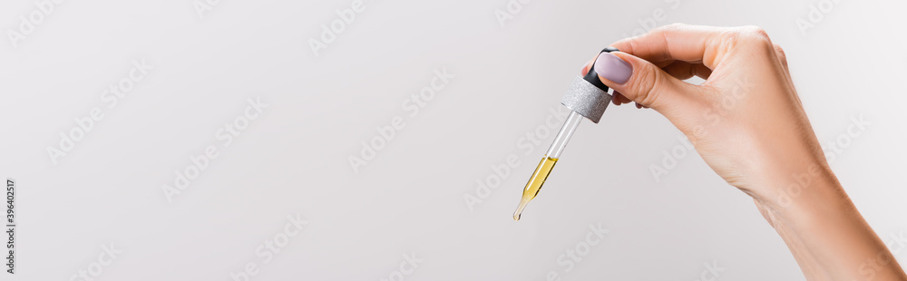 cropped view of woman holding pipette with oil isolated on grey, cropped view of woman holding pipette with oil isolated on grey,