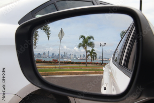 car rear view mirror with image of palm tree and city in the background