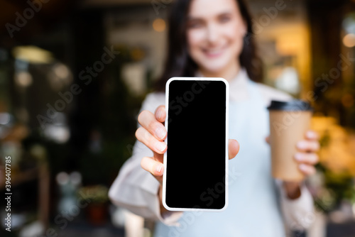 young florist holding smartphone with blank screen and coffee to go on blurred background