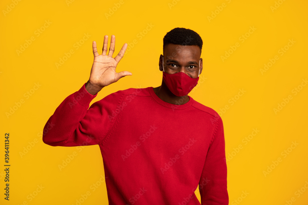 Naklejka premium Positive black guy in red protective face mask waving hand at camera