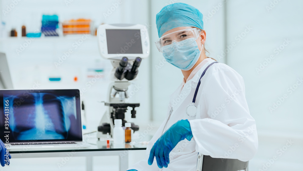 female doctor in a protective mask sitting at a laboratory table.