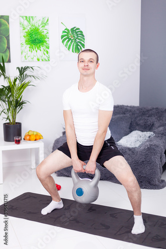 Young man, guy goes in for sports with kettlebell and dumbbells at home