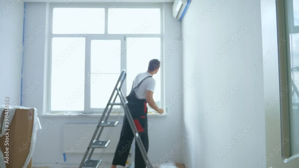 blurred background. a man in overalls on a stepladder paints the walls in the room white blurred background. a man in overalls on a stepladder paints the walls in the room white