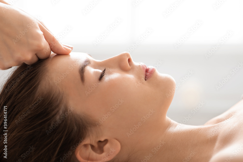 Unrecognizable masseuse massaging relaxed lady forehead, closeup