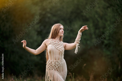Beautiful young woman in beige clothes dancing in a field  macrame in clothes. Blurry background.