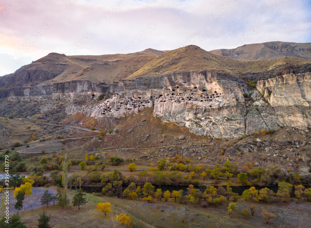 Aerial perspectve of Vardzia-cave city from above with paravani river and autumn nature in foreground. Historical unesco sites Georgia.