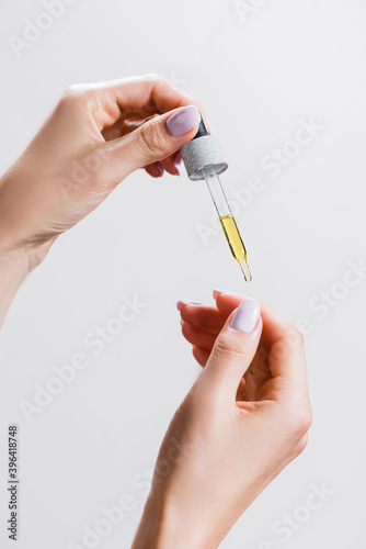 cropped view of woman applying oil from pipette on fingernails isolated on grey, stock image photo