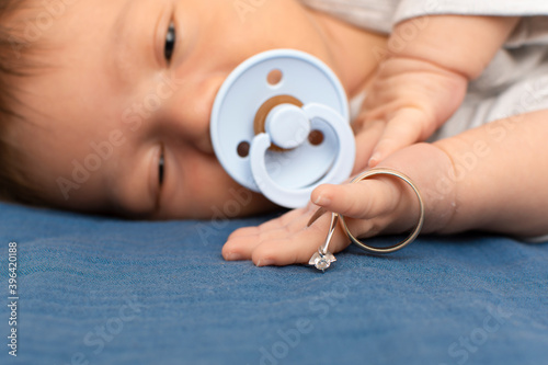 Closeup of newborn baby lying on the bed with parents wedding rings together Happy Family concept. Beautiful newborn photo. Sweet boy sleeps in a bed in nursery. First days of life One week old baby 