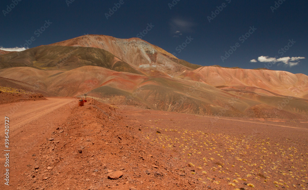 Travel and explore. Driving along the dirt road across the mountain arid desert. View of the route, red land, volcanic landscape, valley and mountains, very high in the Andes cordillera. 