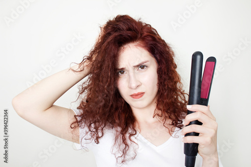 Curly hair. Beauty Close-up of girl with blowing hairstyle holding straightening iron. Glamour fashionable female isolated on white background.