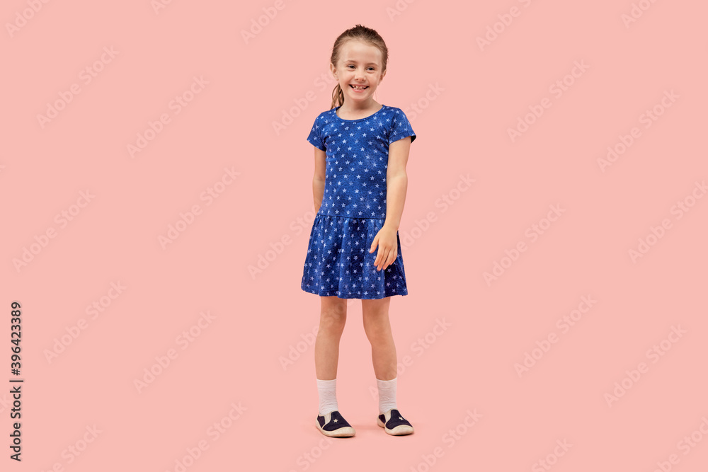 Little brunette girl dancing in a blue dress with a little star print in sneakers. Pink isolated background. Little brunette girl dancing in a blue dress with a little star print in sneakers. Pink isolated background.