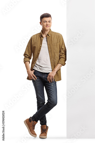 Schilderij op canvas Full length portrait of a young man in shirt and jeans leaning on a wall