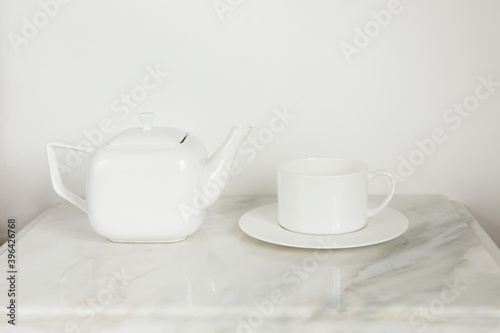 white ceramic tea pot and white tea cup on a white plate on marble coffee table 
