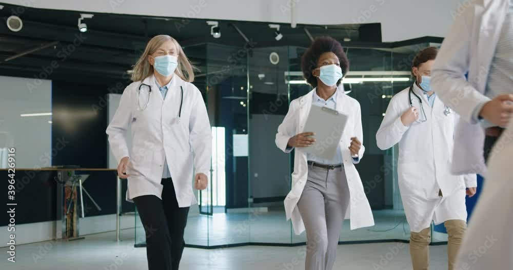 Mixed-races male and female doctors wearing masks using tablet running in medical center in urgent situation. Coronavirus emergency panic in hospital at work. Covid-19. Healthcare concept