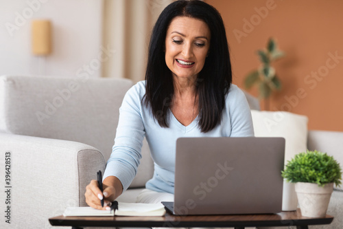 Mature woman writing report working on laptop at home © Prostock-studio