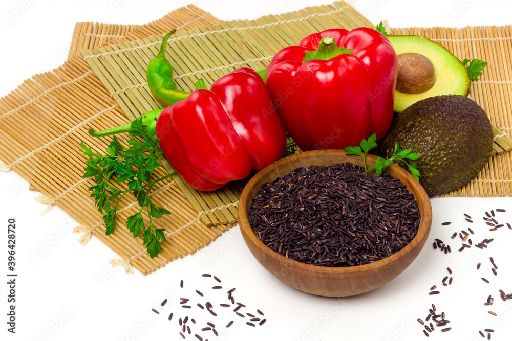 Black rice in wooden bowl and fresh vegetables on sushi bamboo mat. Organic food concept. Eastern culinary ingredients Black rice in wooden bowl and fresh vegetables on sushi bamboo mat. Organic food concept. Eastern culinary ingredients