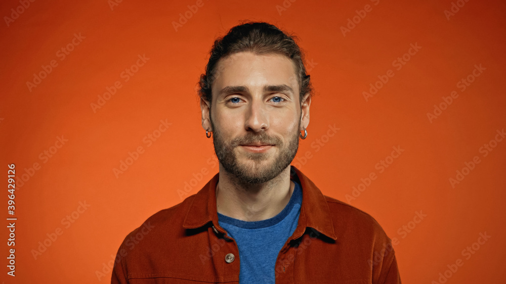Obraz premium pleased bearded man looking at camera on orange background