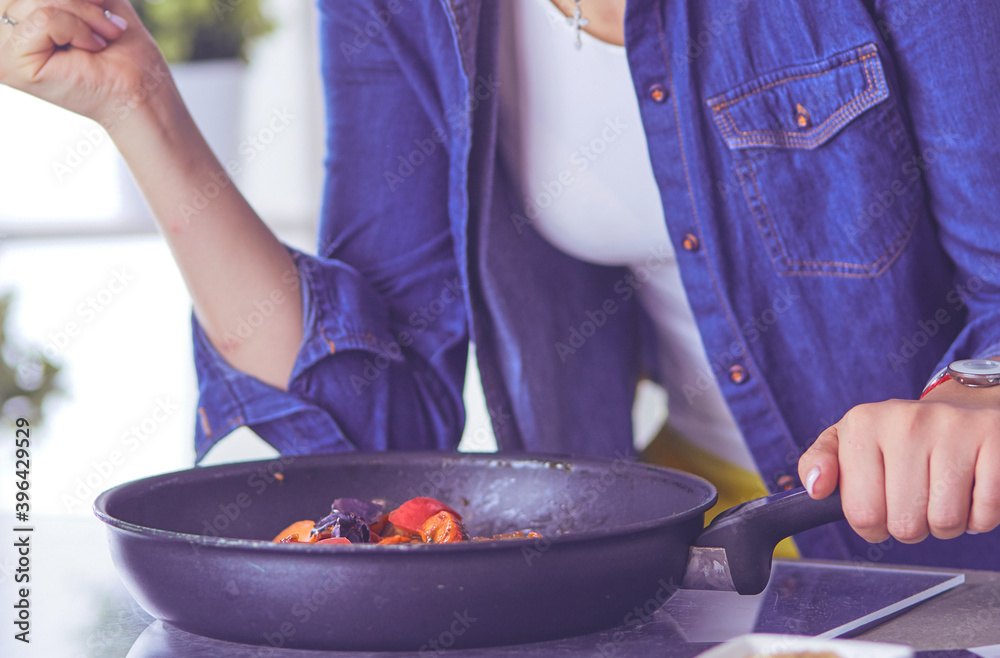 Young woman cooking healthy food holding a pan with vegetables is it. Healthy lifestyle, cooking at home concept