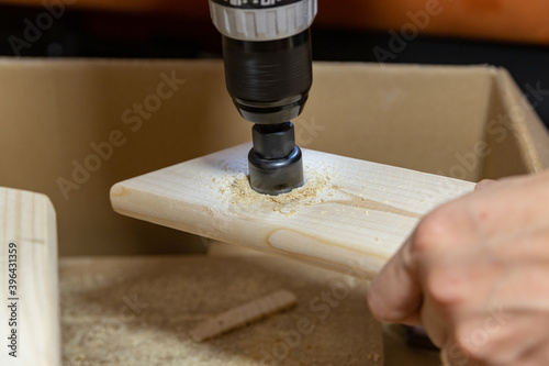 man drills a hole in a wooden board on a box at home handmade