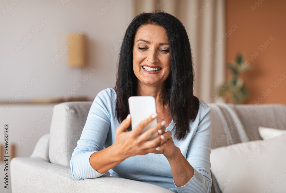 Smiling mature woman using smartphone at her home Smiling mature woman using smartphone at her home