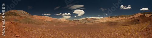 Traveling across the volcanic Andes desert very high in the cordillera. View of the dirt road along the dry valley. The brown land, yellow grasses, and colorful mountains under a beautiful sky.