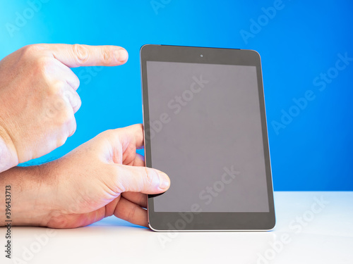 Fototapeta Naklejka Na Ścianę i Meble -  The man points to the tablet screen. Using a tablet PC. Convenient technical gadgets. Men's hands and a tablet with a blank screen. A digital tablet with space for text on the screen.